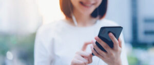 smiling asian woman using smartphone with listening music standing office building_2034 1563